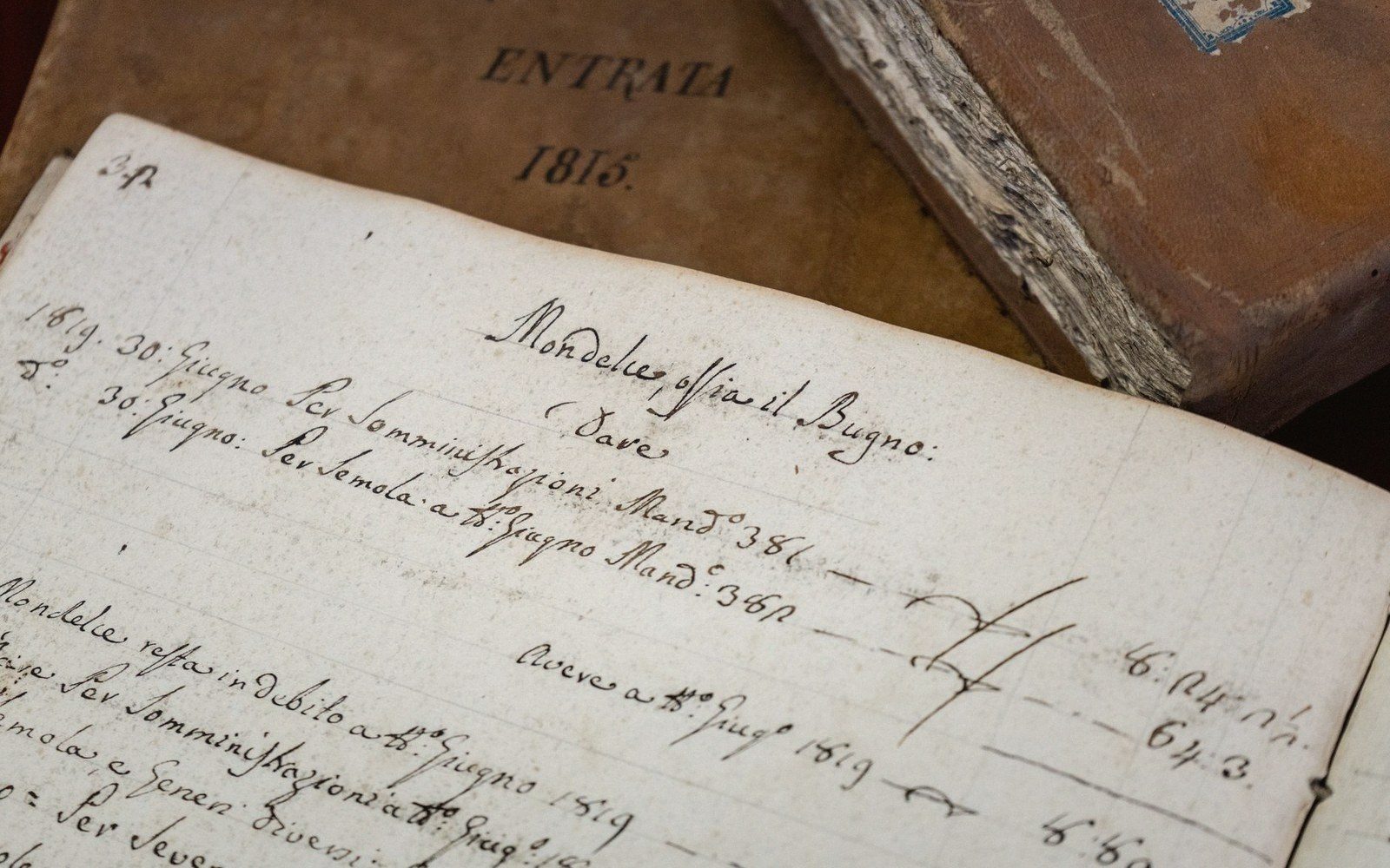 An open ledger page with handwritten Italian entries dated 1815, resting atop a bound volume