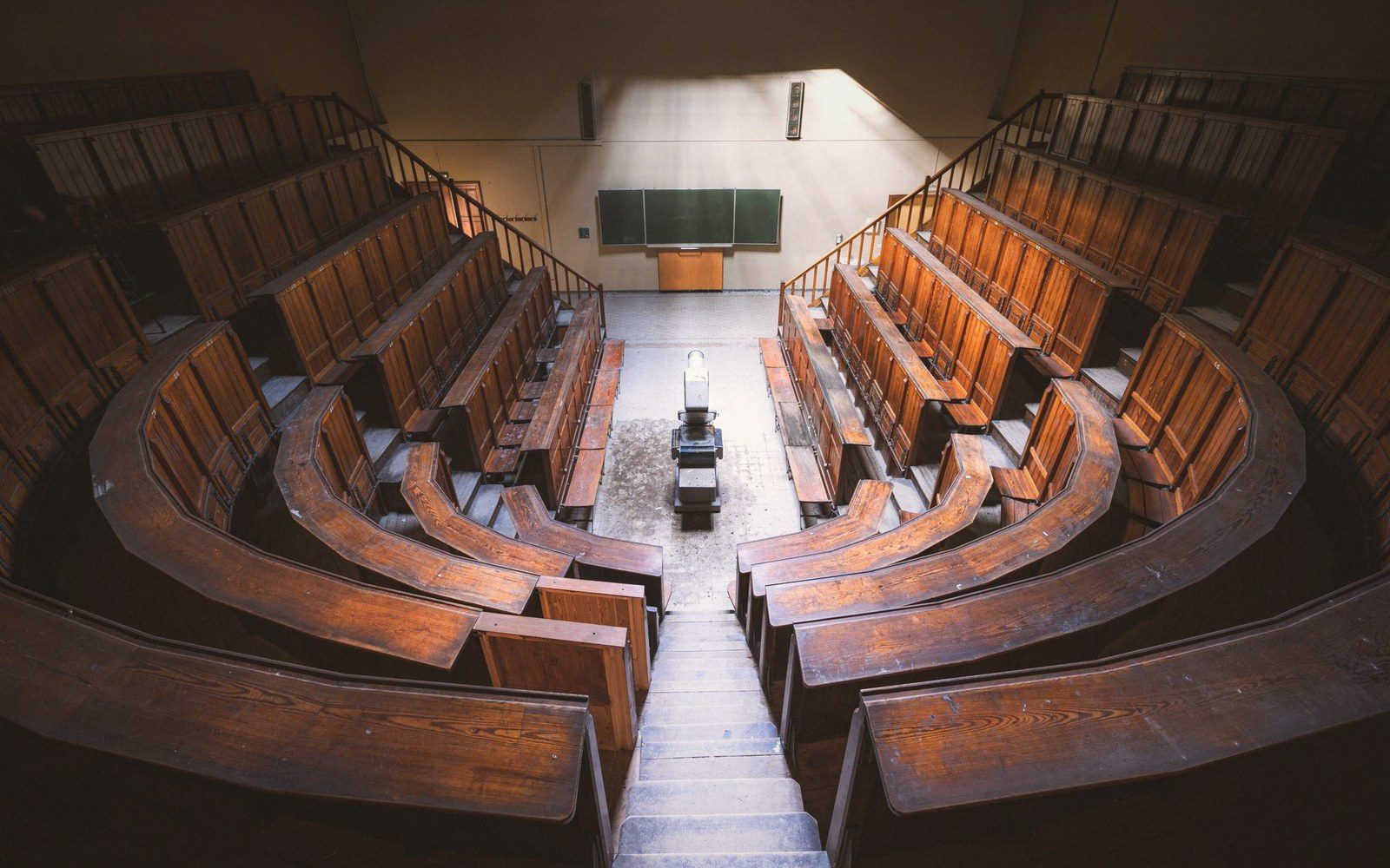A raked university lecture theatre with tiered wooden seating, no occupants, lit from above